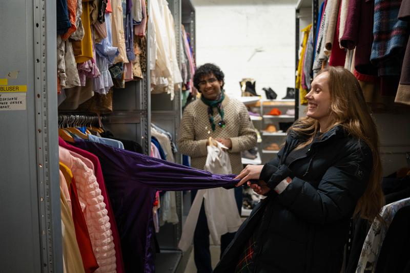 Danial Mirh og Nora Rønning_4K-09318.jpg En gutt og en jente står mellom klær som henger på et kostymelager.